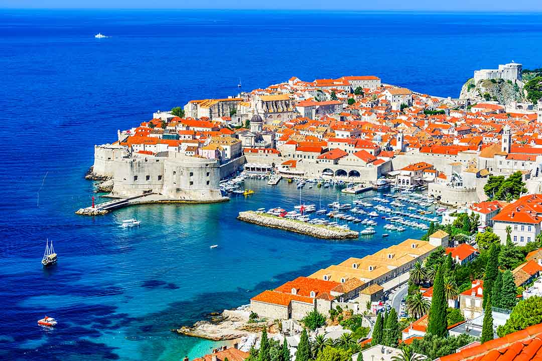 Panoramic view of Dubrovnik Old Town, with terracotta rooftops, historic city walls and the harbour beside the blue Adriatic Sea, Croatia
