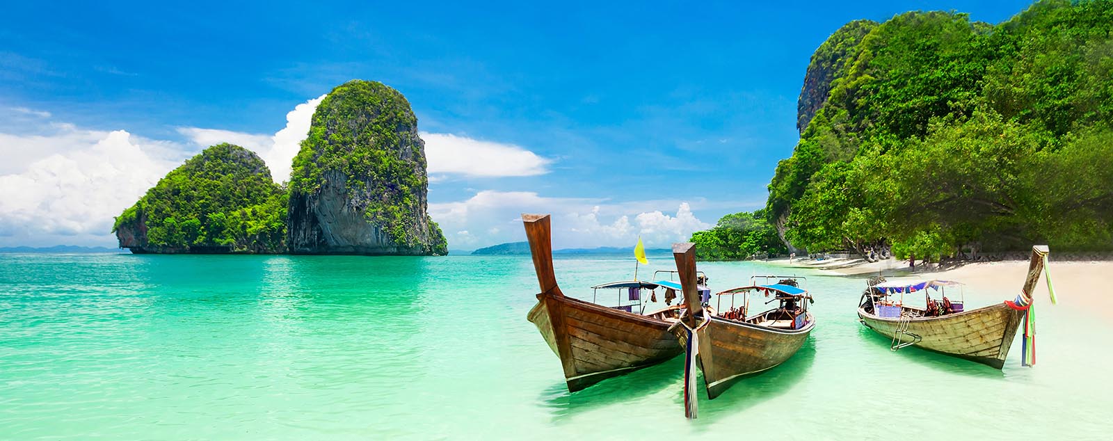 Beauty turquoise waters, white sands and towering limestone cliffs with longtail boats n the foreground, Krabi