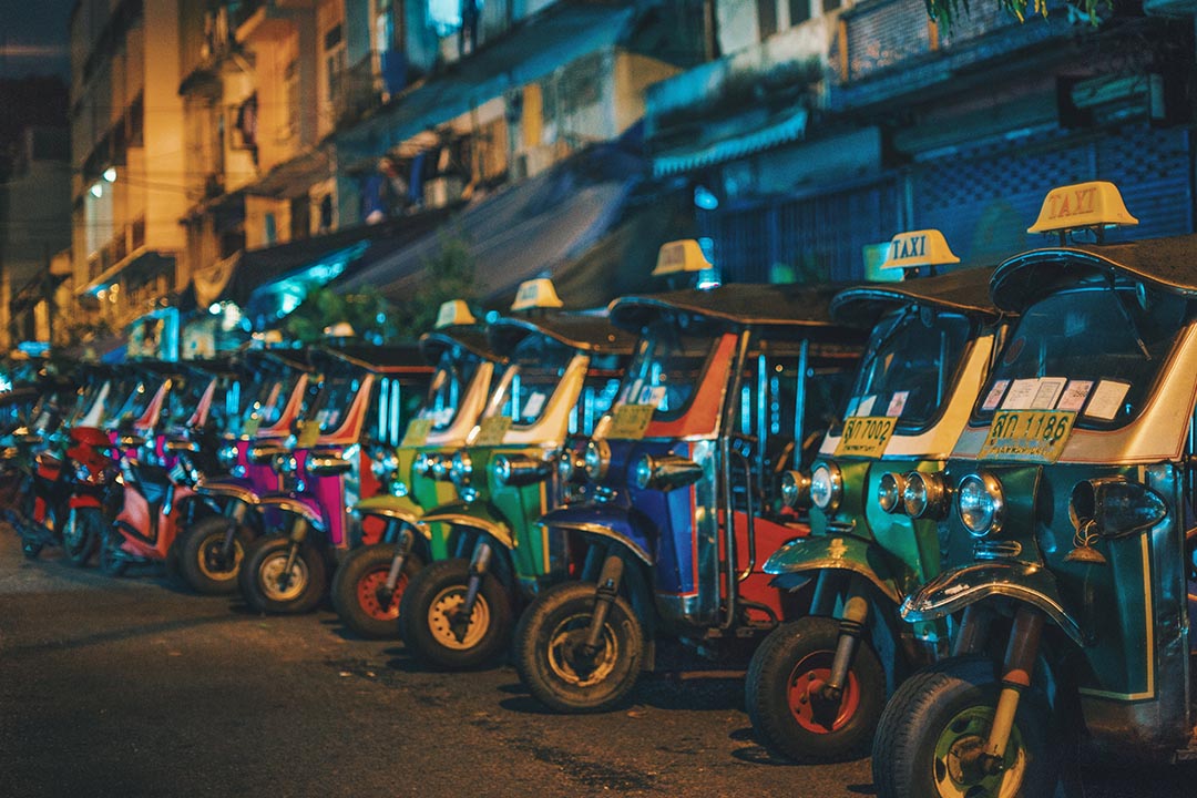 Brightly coloured Tuk Tuk's lined up together on a street.