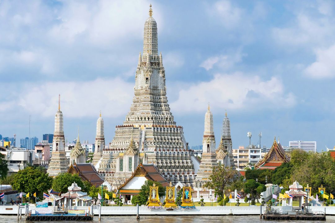 Wat Arun temple An intricately decorated white temple with a central tower and four satellite towers around sits on the bank of a river