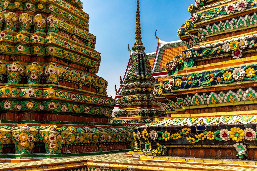 Wat Pho temple, Bangkok Ornate, colourful stupas at Wat Pho in Bangkok, decorated with intricate floral mosaics against a bright blue sky.