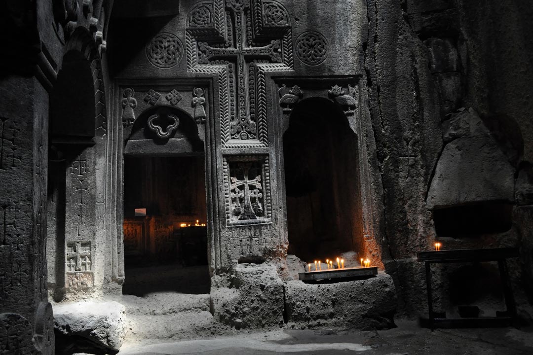 A crucifix is carved into the wall of an old stone church that is lit by candlelight