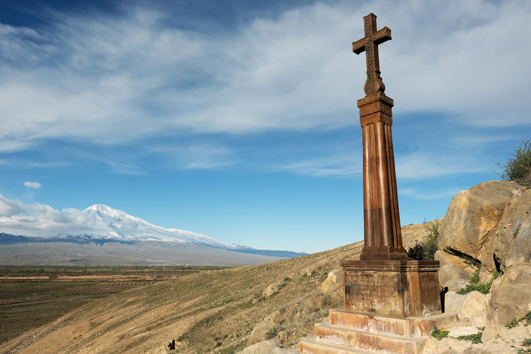 A statue of the crucifix stands alone with vast plains and then a snow topped mountain in the distance