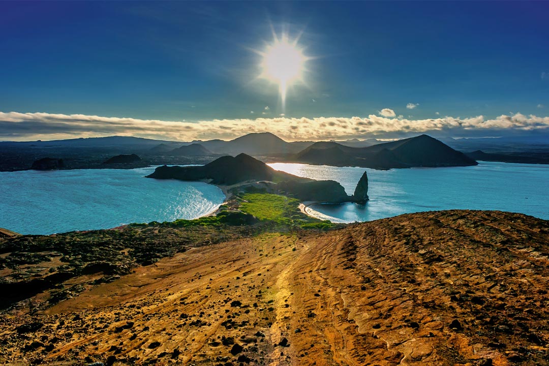 A view with the sun in the sky, blazing over some of the Galapagos islands, surrounded by blue waters