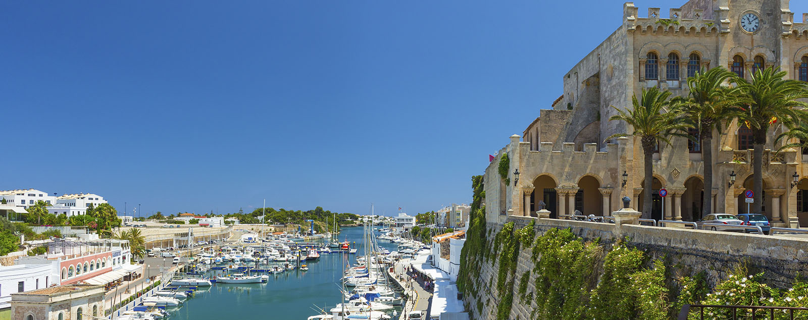 A view across the harbour in Ciutadella. A large and grand building stands over looking boats bobbing in the water