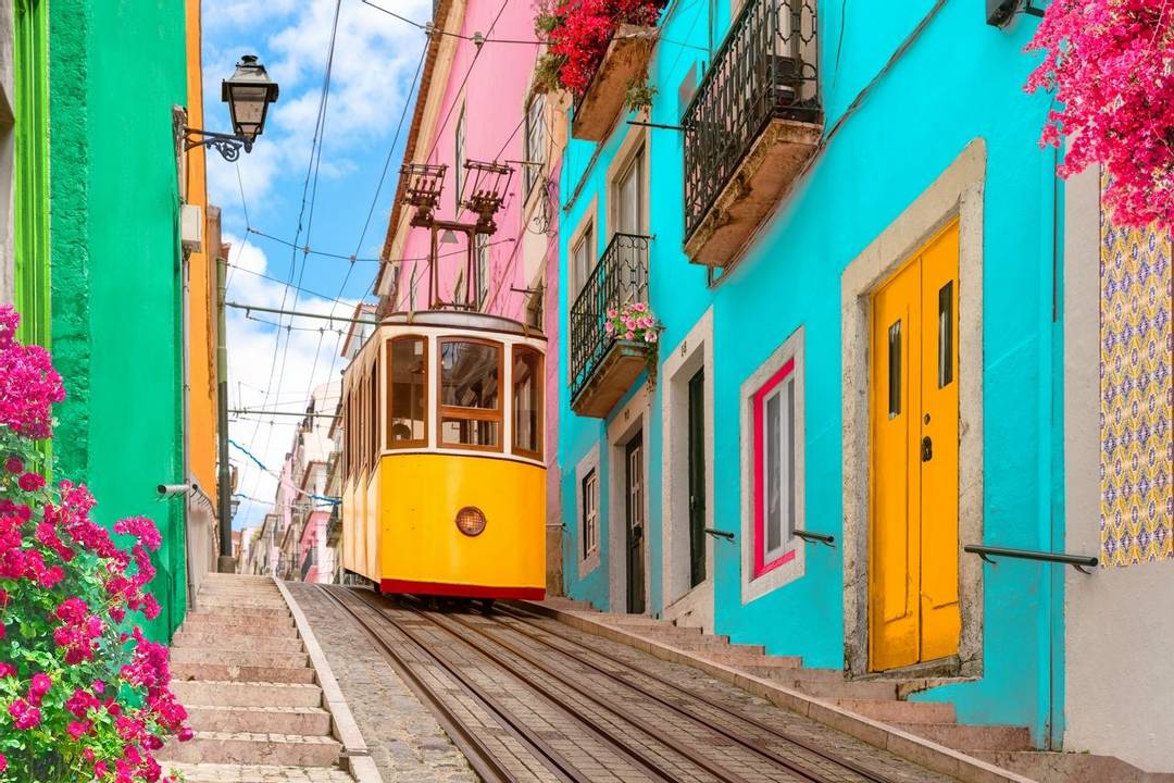 A steep street in Lisbon lined with buildings in bright colours with a yellow tram in the centre