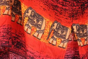 A close up of red fabric with elephants with intricate patterns printed on it walking in a line