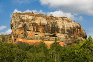 A large rock with streaks of sediment markings sit at the top of a high ridge with a lush forest below
