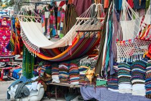 Vibrant multi coloured hammocks hanging up and other brightly coloured woven items on a market stall