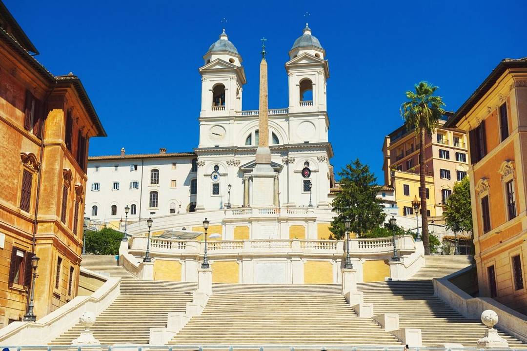 The Spanish Steps A wide set of stone white steps in three sections lead upwards then sweep left and right round to a white church with two tall bell towers with a central monument in front