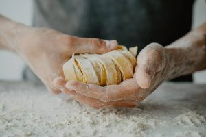 A close-up of flour-covered hands holding tagliatelle pasta strips