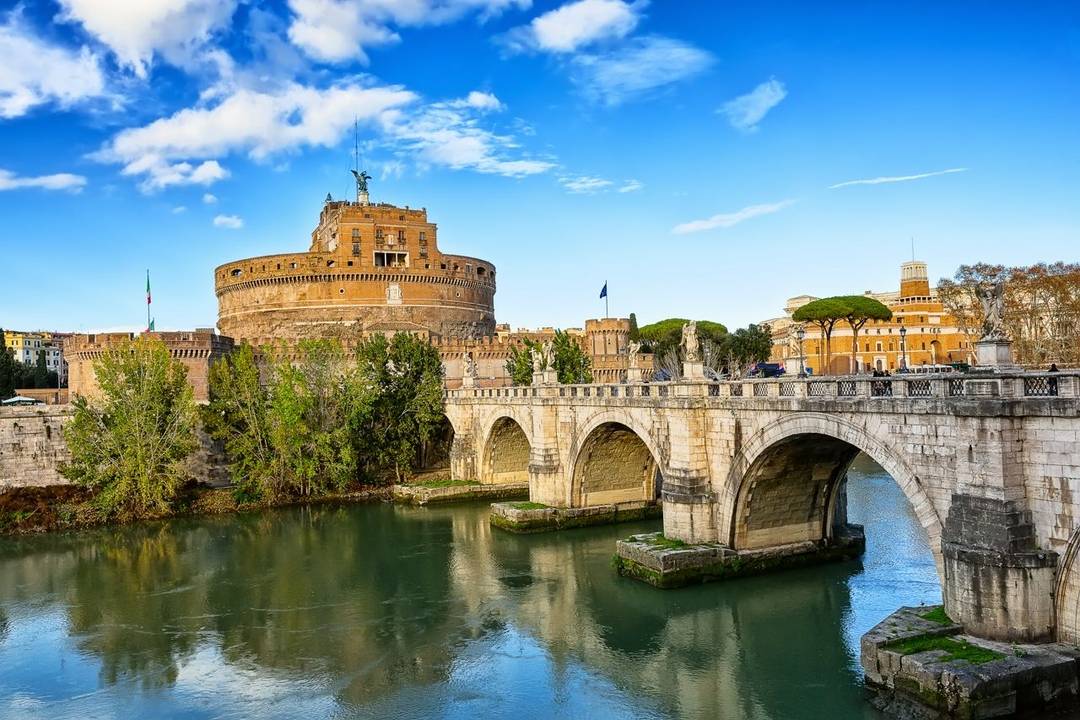 Stone multi arched bridge over the Tiber River, leading towards a circular castle