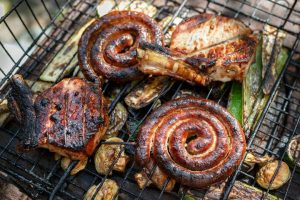 Swirled sausages, chops, mushrooms and courgettes all cooking on a barbecue or 'braai'