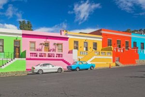 A line of bright green, pink, yellow, red and turquoise blue houses with a turquoise blue and white car outside.