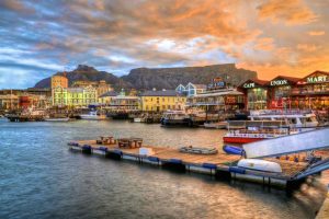 Sunset over a colourful harbourside with neon lit restaurants and table mountain in the background