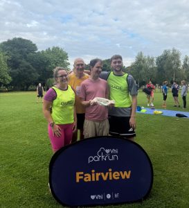 Tom and his park run crew stand in front of the parkrun sign
