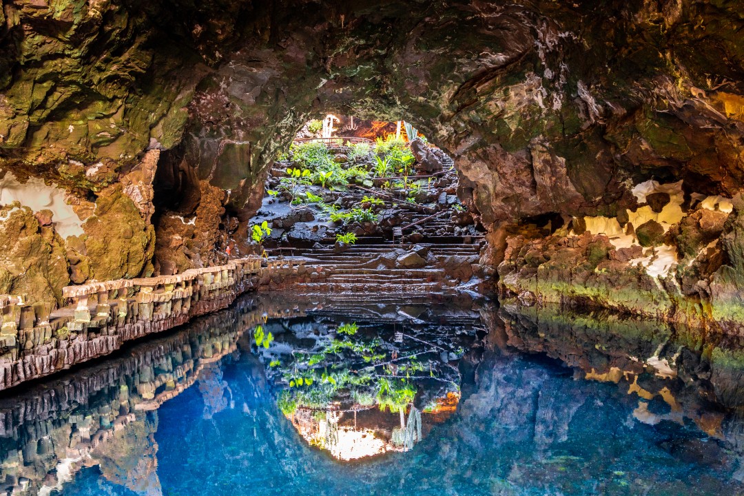 A striking volcanic cave transformed by César Manrique into an atmospheric blend of lava rock, still water, tropical plants and art