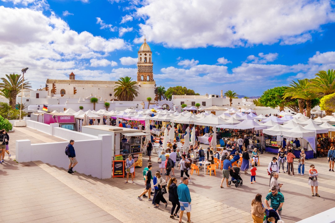 Bright blue skies over a busy market, with stalls selling colourful craft items,