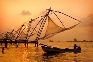 The orange sun sets behind traditional fisherman in Kochi