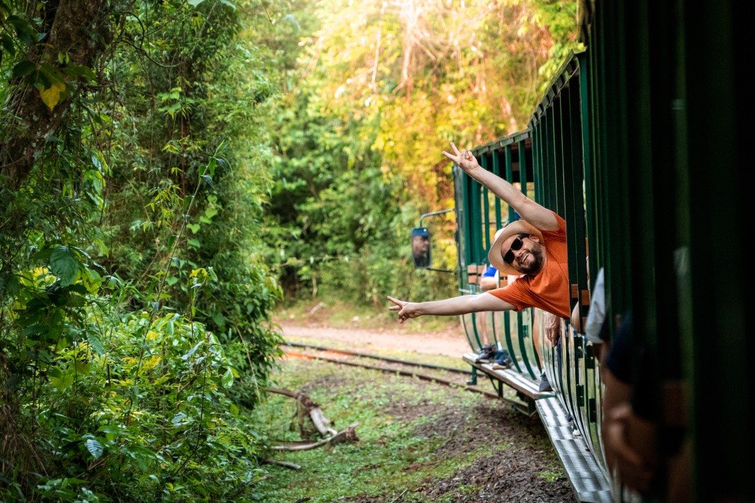 Ecological train to Devil’s Throat Traveller leaning from an open-sided ecological train travelling through tropical rainforest towards Devil’s Throat in Iguazú National Park