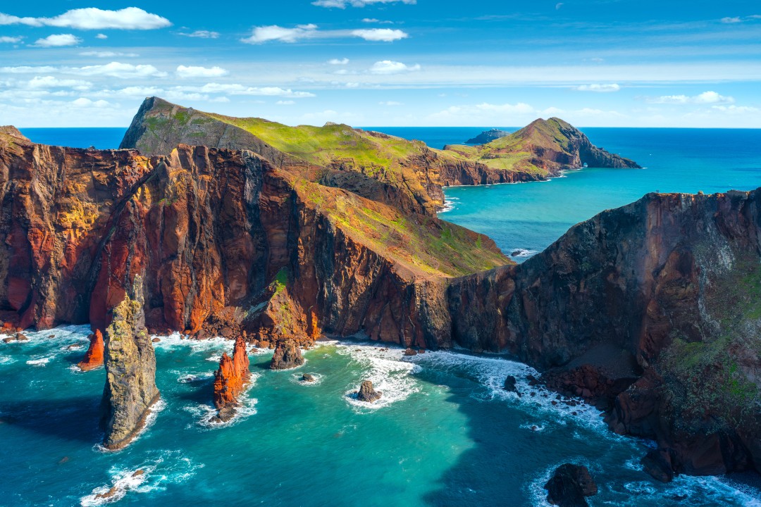 Rugged red and black volcanic cliffs and sea stacks surrounded by turquoise Atlantic waters at Ponta de São Lourenço