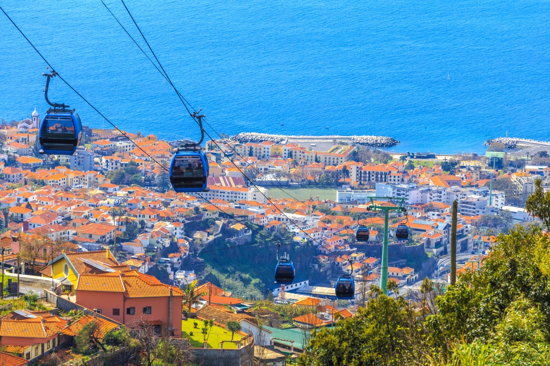 Cable cars travelling above Funchal’s orange-roofed buildings towards the blue Atlantic Ocean, Madeira