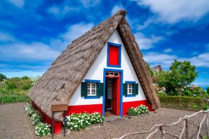 Traditional triangular thatched house with a steep straw roof, colourful painted doorway and flower beds in Santana