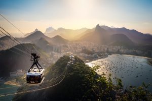 Cable car travelling above forested hills with Botafogo Bay, Rio de Janeiro and Christ the Redeemer visible in the distance