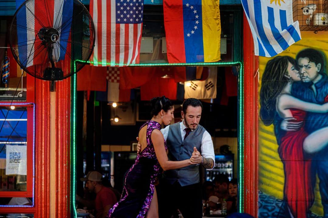 Tango dancers outside a restaurant Couple performing the tango outside a restaurant, framed by colourful signs, flags and a mural