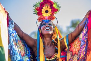 Woman demonstrating a colourful Brazilian Carnival costume with a floral headdress, flowing ribbons and brightly patterned fabric
