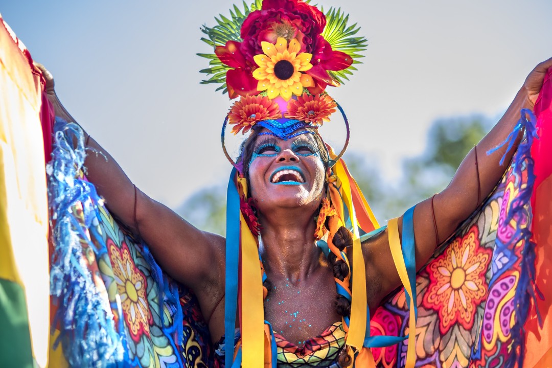 Woman demonstrating a colourful Brazilian Carnival costume with a floral headdress, flowing ribbons and brightly patterned fabric