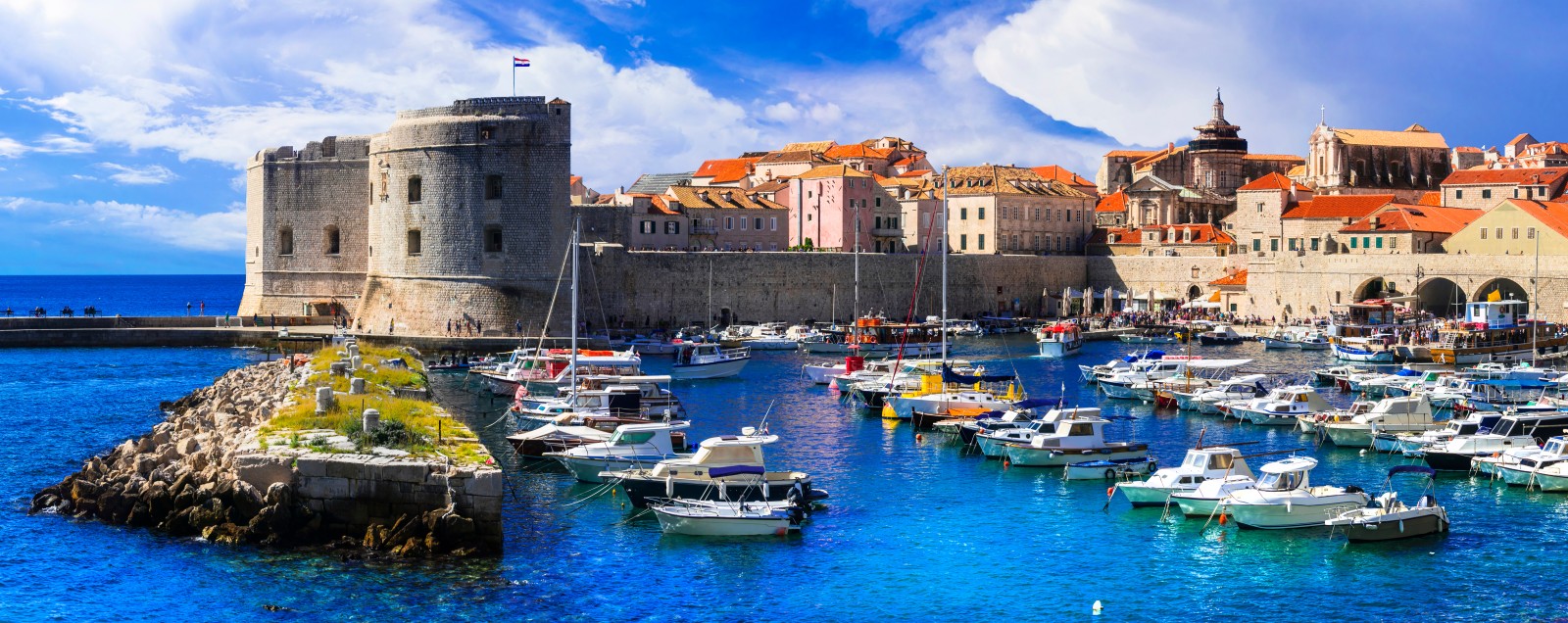 Dubrovnik Old Port with boats in the harbour, historic city walls and St John Fortress overlooking the Adriatic Sea, Croatia