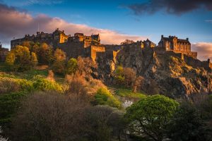 Edinburgh Castle rises above trees and rocky slopes in a warm evening light
