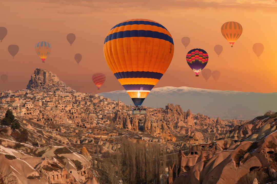 Hot-air balloons floating above Cappadocia’s rocky valleys and cave settlements at sunrise, Cappadocia