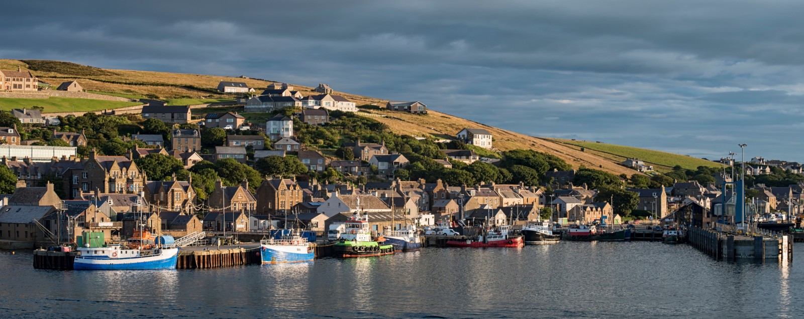 Fishing boats moored in Stromness Harbour with stone houses rising behind, Orkney Islands