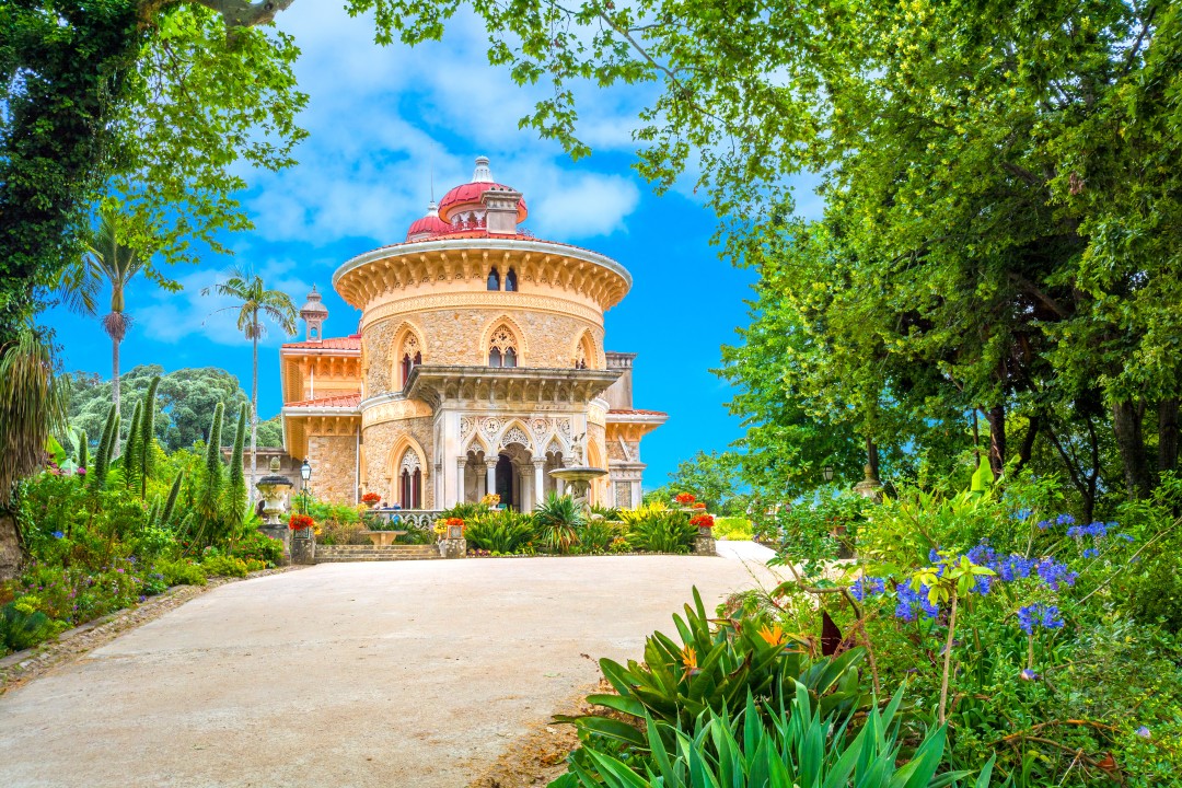 Monserrate Palace and Gardens Monserrate Palace and Gardens including a circular tower and red domed roof, surrounded by lush green trees and flowering plants in Sintra