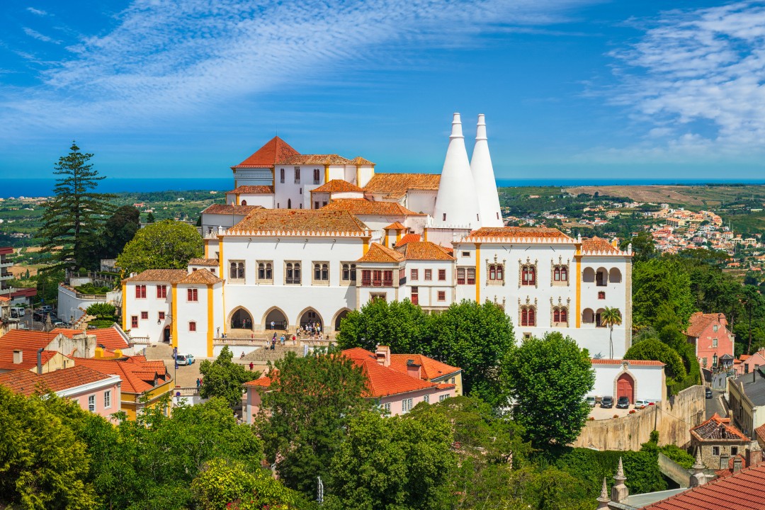 Sintra National Palace with two distinctive conical chimneys, terracotta roofs and green trees beneath a blue sky