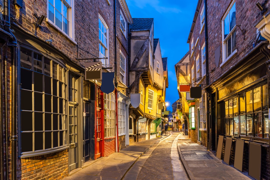 Narrow cobbled street lined with medieval timber-framed buildings and illuminated shopfronts along The Shambles at dusk, York