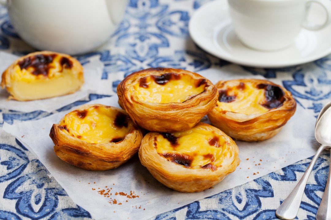 Portuguese Pastéis de Nata Portuguese custard tarts with golden flaky pastry and caramelised tops, served on a blue and white patterned tablecloth