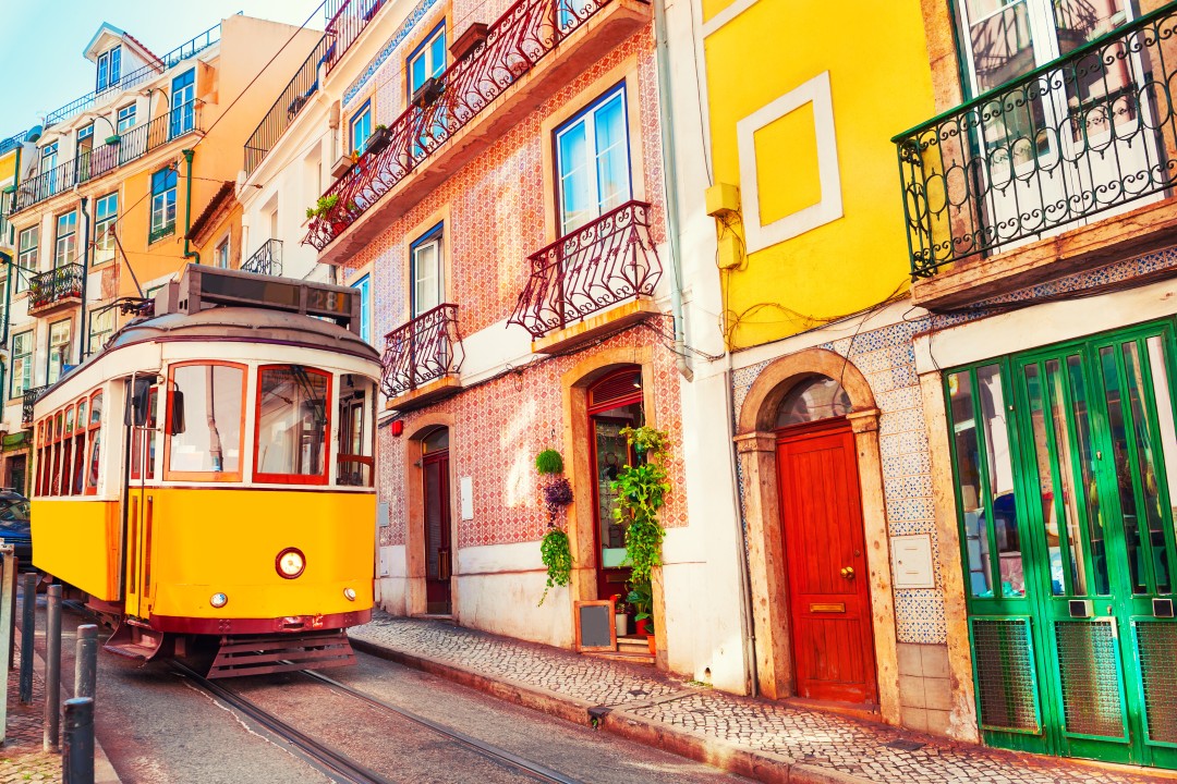Traditional Lisbon Tram Yellow and white vintage tram travelling along a narrow cobbled street lined with colourful buildings, tiled facades and wrought-iron balconies in Lisbon
