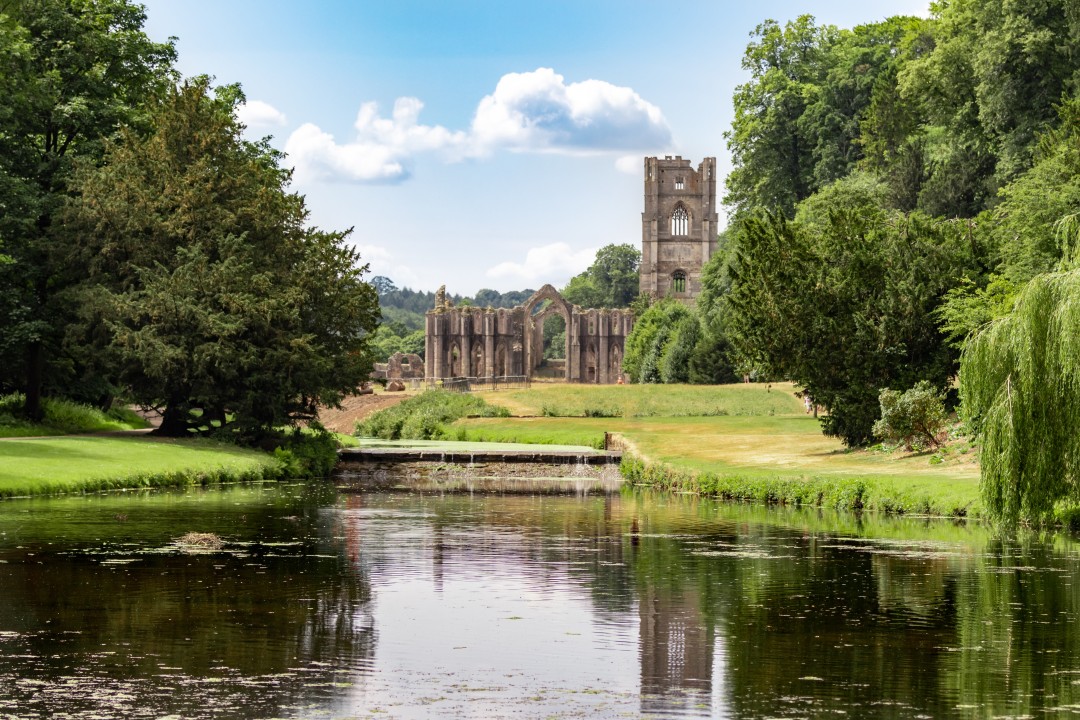 Fountains Abbey & Studley Royal Water Garden, North Yorkshire Medieval ruins of Fountains Abbey beyond a tranquil lake, framed by green lawns and mature trees at Fountains Abbey and Studley Royal Water Garden