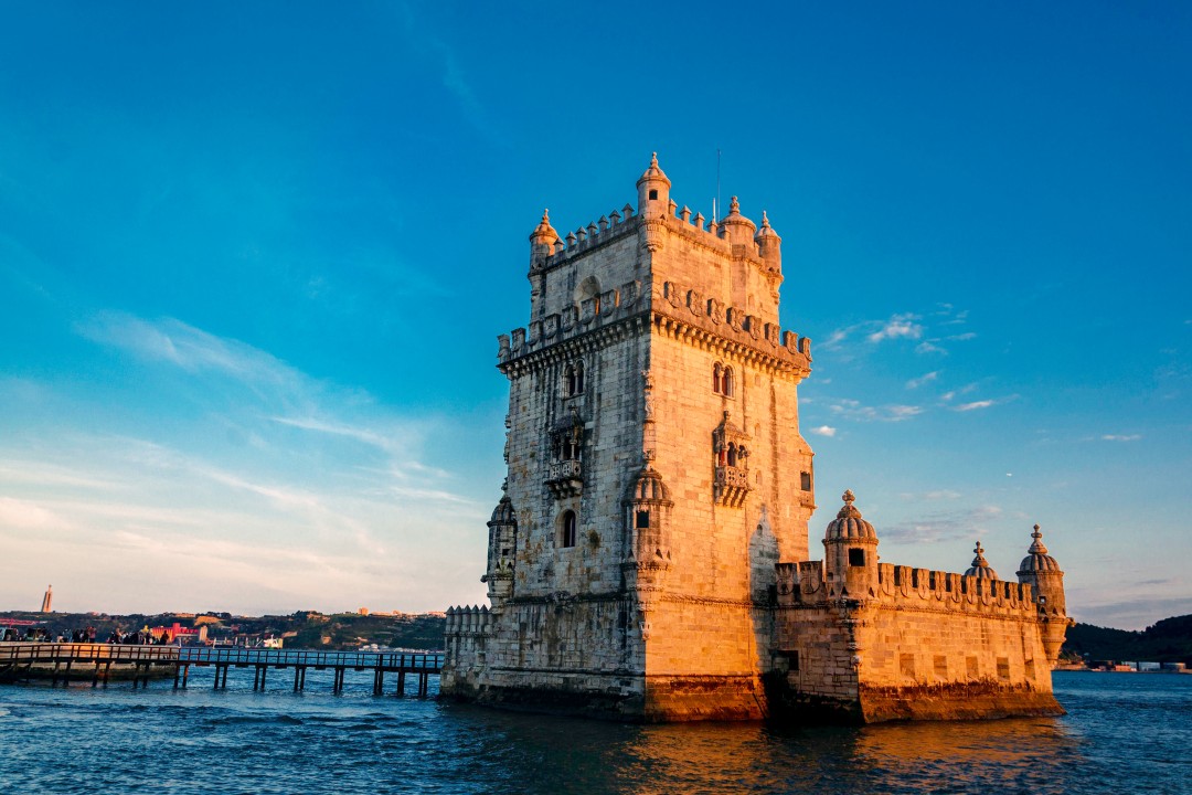 Belém Tower Historic stone tower with ornate battlements standing in the River Tagus, illuminated by warm sunlight beneath a blue sky in Belém, Lisbon